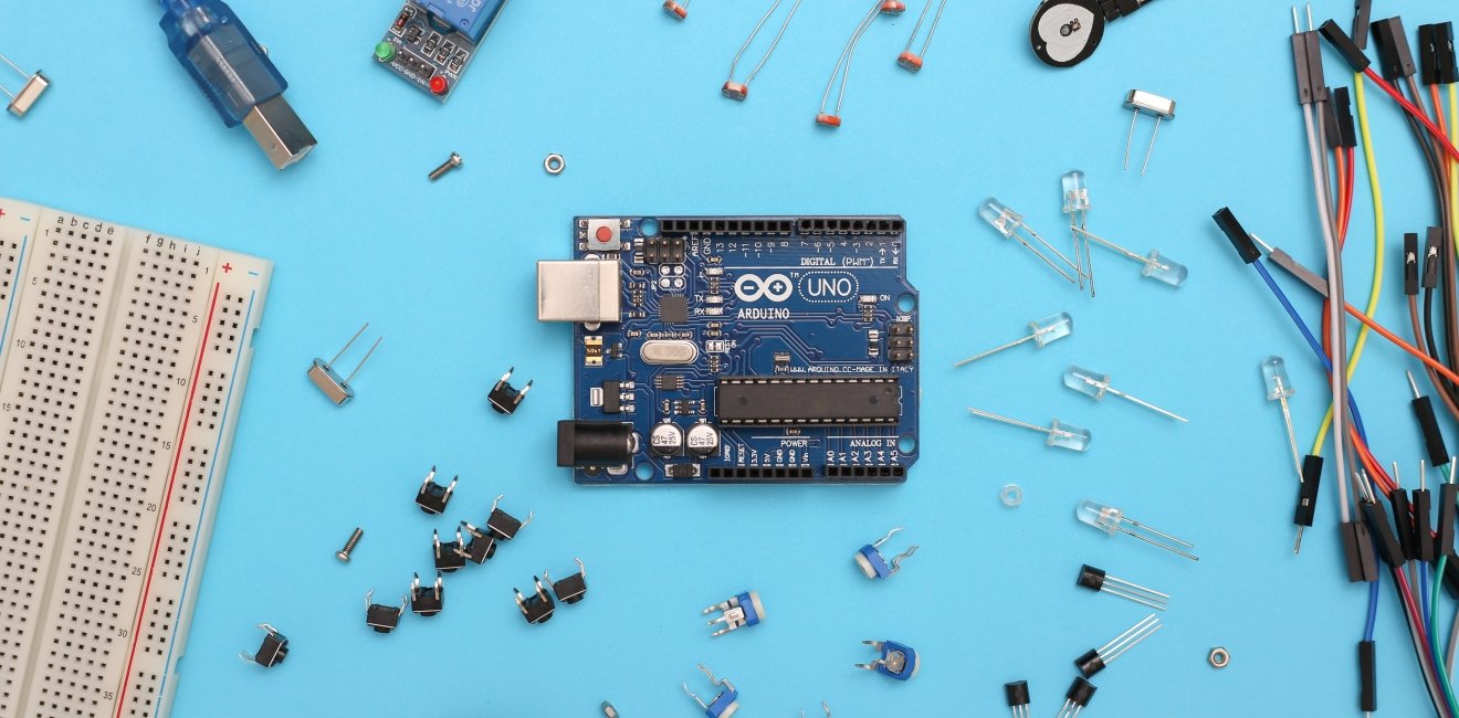 blue and black circuit board Arduino Uno and electronic parts on a blue surface.