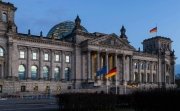 The Bundestag building at dusk, with German and EU flags waving in front.