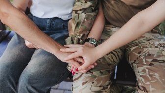 Group holding hands with a uniformed service member in camouflage..