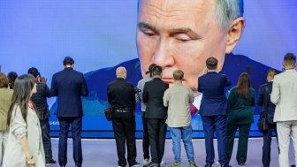 A crowd of people take pictures and watch a largescreen broadcast of President Vladimir Putin.