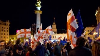 A crowd of protesters in front of the monument in Liberty Square in Tbilisi wave Georgian flags and EU flags.