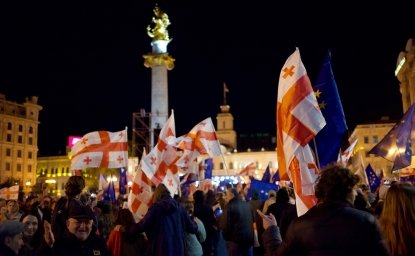 A crowd of protesters in front of the monument in Liberty Square in Tbilisi wave Georgian flags and EU flags. 