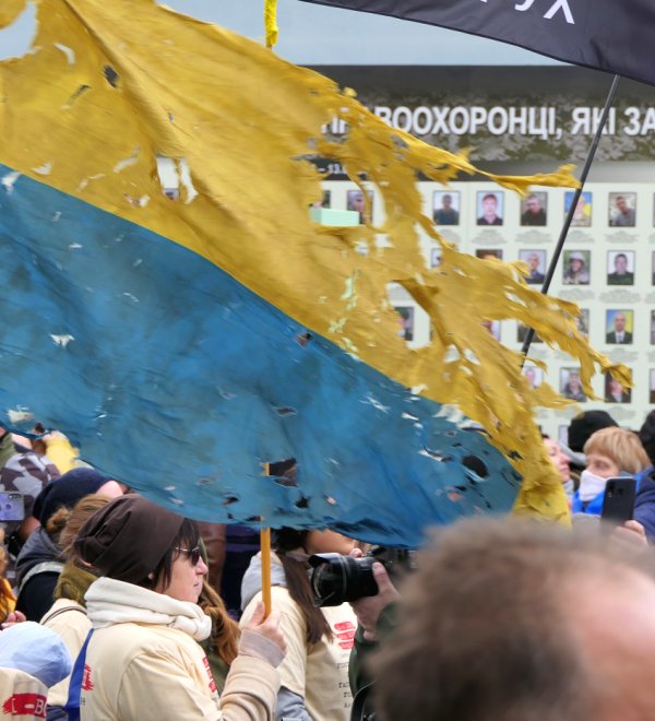 a tattered Ukrainian flag flies above a crowd of people