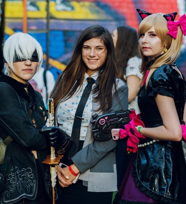 Three women dressed in fantasy and punk costumes standing in front of a mural at a festival in Kyiv