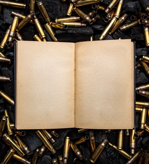 open book in a black hardcover with yellowed blank pages. Empty gun cases lying on charred coals.