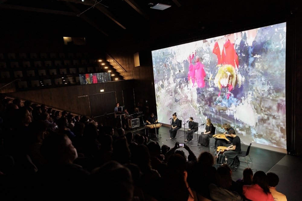 Audience watching a musical performance with abstract image in background of stage