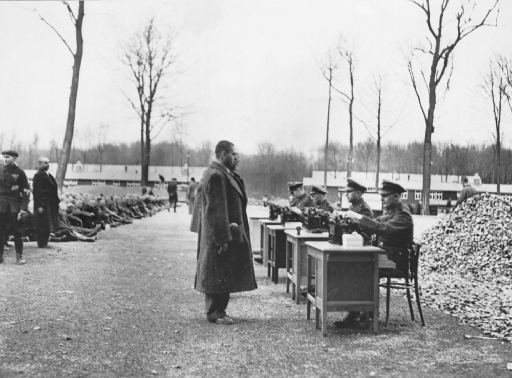 Gestapo officials recording data on incoming prisoners at a German concentration camp. Many others are seated on the ground