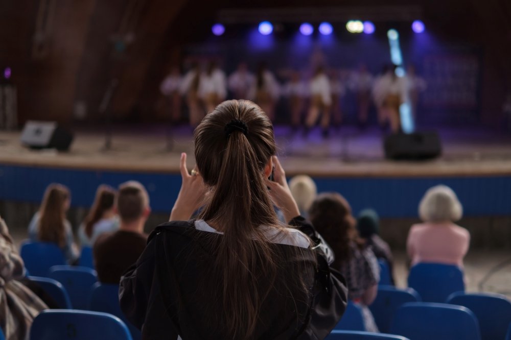 Girl taking a photo of dancers on the stage. 