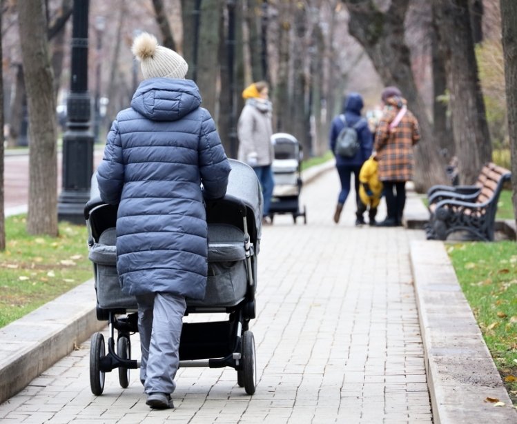 Mothers walking with baby prams on city street at autumn. Woman with stroller for twins in foreground