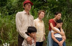 A family of five people stand in a wooded area.