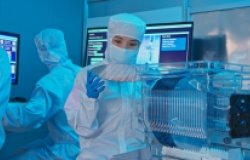 A woman in a clean suit holds up a silicon wafer in a laboratory.