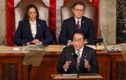 Prime Minister Kishida stands at a lecturn giving a speech, Vice President Harris and Speaker Johnson are seated behind him.