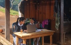 Two girls sitting in front of a computer in the rural outdoors.