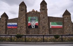 Portrait of Akhmad Kadyrov on a old stone building next to Russian and Chechen Flags